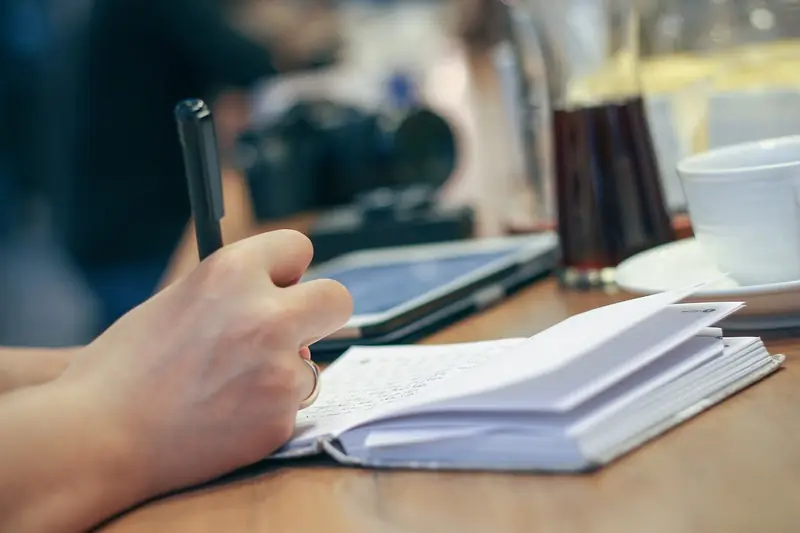 A hand writing notes in an open notebook with a pen, suggesting analysing and annotating a chess game.