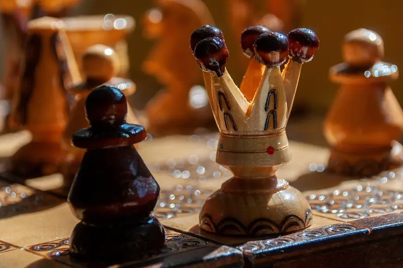 Close-up of wooden chess pieces, including the queen, on a board mid-game in warm light.